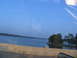 1995 Ford C-350 (Centurion Conversions) - A boat is docked near a small island with trees, viewed from a moving vehicle on a clear day.