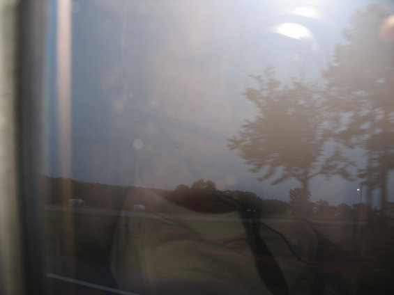 Reflection of trees and sky in a window, with a blurry landscape outside