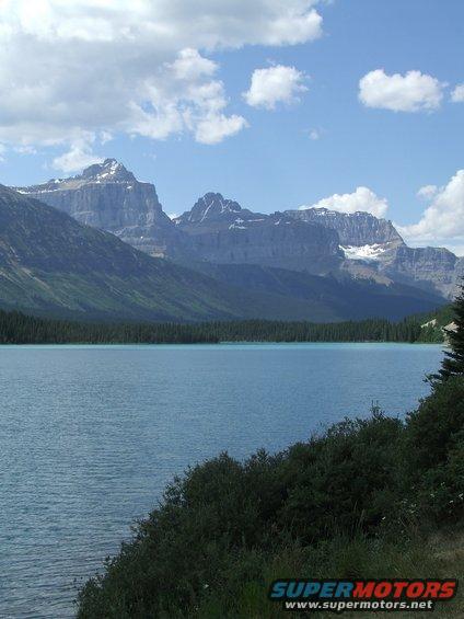 Mountain range overlooking a blue lake with trees and clouds