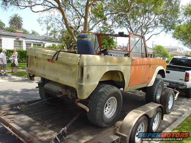 1977 Ford Bronco on trailer, orange and tan, missing parts, with white pickup truck behind