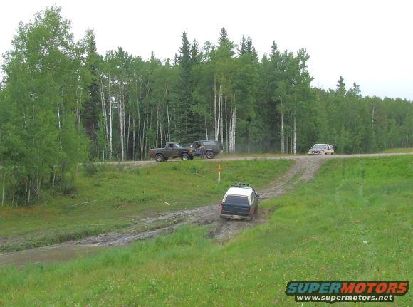 Dark blue and white Ford Bronco driving on a muddy track, rear view