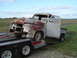 1955 Ford F-100 - A heavily rusted 1955 Ford F-100 truck is being transported on a trailer, missing its front grille and headlights.