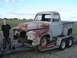 1955 Ford F-100 - A young man stands beside a weathered 1955 Ford F-100 pickup truck being transported on a U-Haul trailer.
