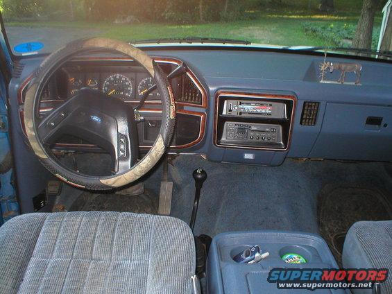 1989 Ford Bronco interior with camo steering wheel cover, blue seats, and aftermarket radio