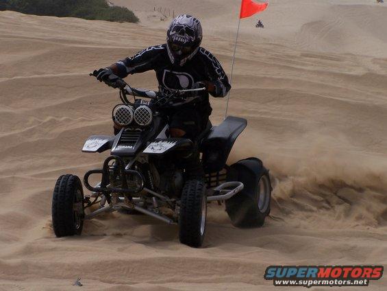 Black ATV with skull helmet rider kicking up sand