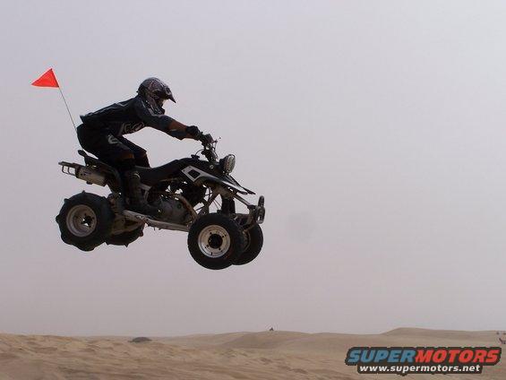 Quad bike with rider jumping over sand dunes, orange flag on back