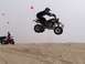 1999 Yamaha WARRIOR - A rider on a quad bike performs a jump in a desert landscape with sand dunes and a hazy sky.
