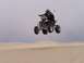1999 Yamaha WARRIOR - A quad bike rider soars through the air during a jump over sand dunes, with an orange flag visible.