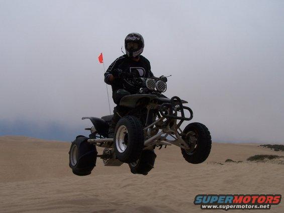 Quad bike rider airborne over sand dunes with an orange flag