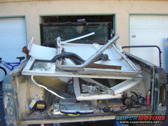 Pile of disassembled vehicle parts, including doors and windows, in the bed of a truck