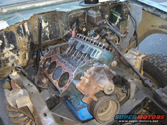 Engine bay with V8 engine disassembled, showing block and cylinder heads. Supermotors.net watermark visible