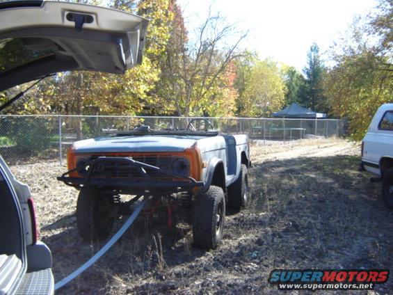 Orange and blue Ford Bronco with a winch cable attached, parked next to a white SUV