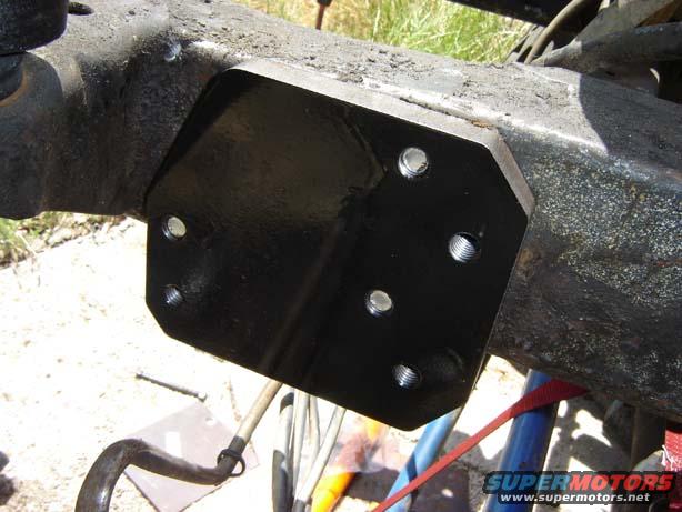 Black metal bracket bolted to a rusty frame section