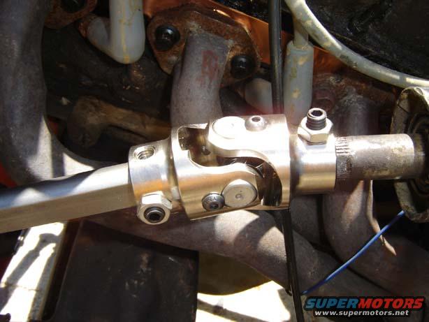 Steering shaft universal joint with bolts and nuts, connected to a splined shaft, surrounded by exhaust pipes