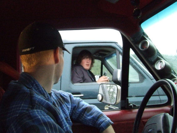 Interior view of a truck cab with a person looking out the window at another person in a different vehicle