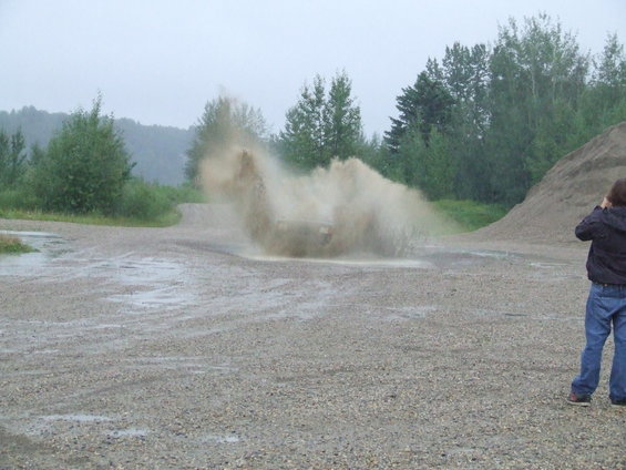 SUV driving through a muddy puddle, kicking up a large spray of water and dirt