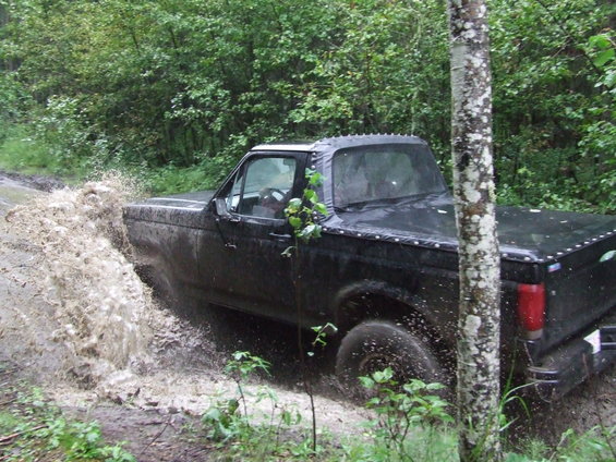 Black 1990s pickup truck splashing through mud on a wooded trail