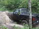 1990 Ford Bronco - A black pickup truck navigates a muddy path, kicking up water and dirt amidst a forest setting.