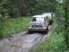 1990 Ford Bronco - A convoy of SUVs navigates a challenging muddy track through a dense forest.
