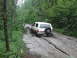 1990 Ford Bronco - A white Ford Bronco navigates a deeply rutted and muddy forest road, kicking up spray as it goes.