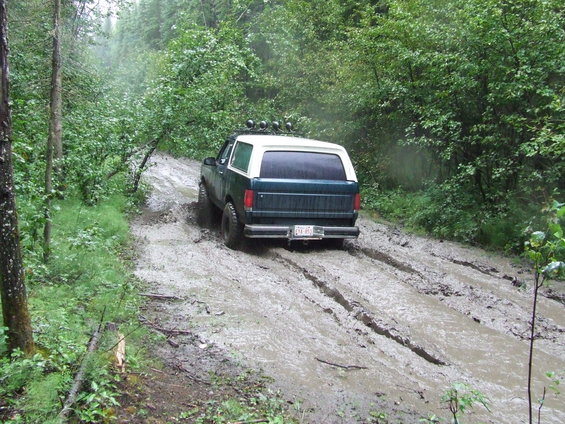 1990 Ford Bronco driving on muddy forest road, rear view