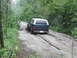 1990 Ford Bronco - A 1990 Ford Bronco navigates a challenging muddy path through a dense forest.