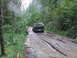 1990 Ford Bronco - Dark green 1990 Ford Bronco navigates a challenging muddy track through a dense forest.