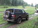 1990 Ford Bronco - A dark green Ford Bronco navigates a muddy off-road trail, with another vehicle visible further up the path.