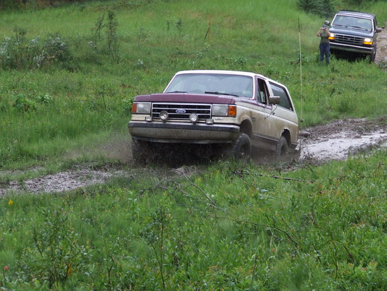Tan and maroon Ford Bronco driving through mud, another SUV behind it