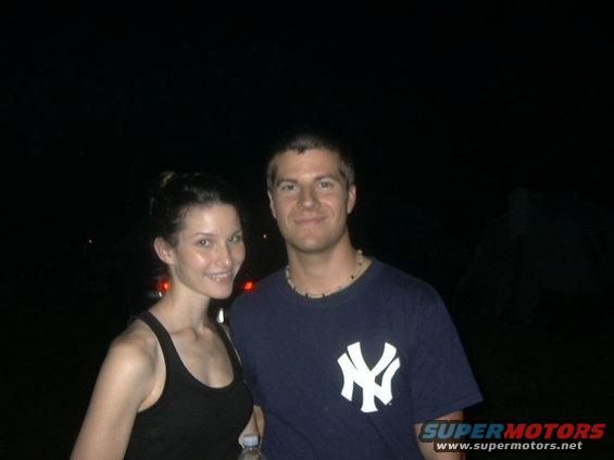 Guy in a Yankees shirt and a woman in a tank top pose for a photo at night. A car is barely visible behind them