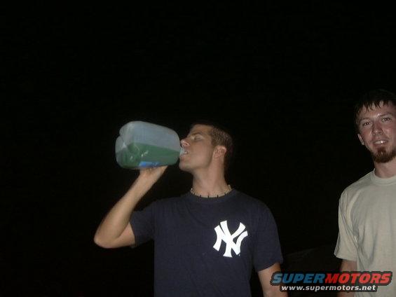 Man drinks from a large jug; another man stands nearby