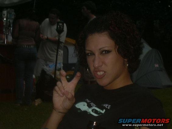 Woman in foreground making peace sign, people and tents in background