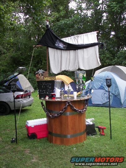 Silver sedan with trunk open, parked next to a wooden bar and tents