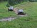 1990 Ford Bronco - Two trucks navigate a muddy trail in a rural, wooded area during daylight.