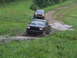 1990 Ford Bronco - Two trucks navigate a muddy off-road trail in a wooded area.