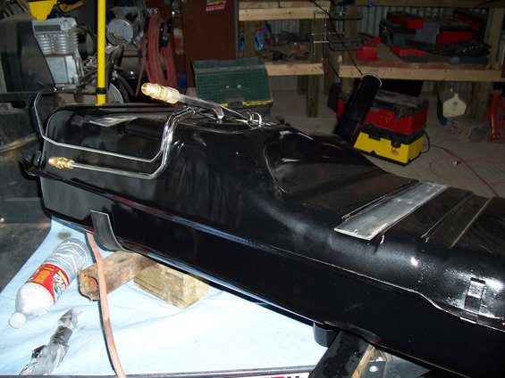 Black fuel tank with metal lines and brass fittings, resting on wooden blocks