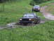 1990 Ford Bronco - Two trucks navigate a muddy trail in a wooded area.