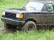 1990 Ford Bronco - Mud-covered black pickup truck navigates grassy terrain.