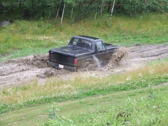 Black pickup truck with a bed cover driving through a muddy track, splashing mud