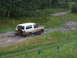 1990 Ford Bronco - A maroon and white Ford Bronco navigates a muddy track through a wooded area.