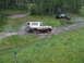 1990 Ford Bronco - A 1990 Ford Bronco navigates a muddy trail, kicking up water as a black pickup truck follows behind.