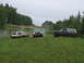 1990 Ford Bronco - Three Ford Broncos navigate a grassy, off-road terrain under an overcast sky.