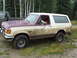 1990 Ford Bronco - A muddy Ford Bronco is parked next to another vehicle in a wooded area.