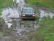 1990 Ford Bronco - A dark SUV navigates a treacherous muddy path, its front end angled downwards.
