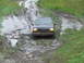 1990 Ford Bronco - A dark SUV, likely a 1992 Ford Bronco, struggles through a challenging muddy terrain.