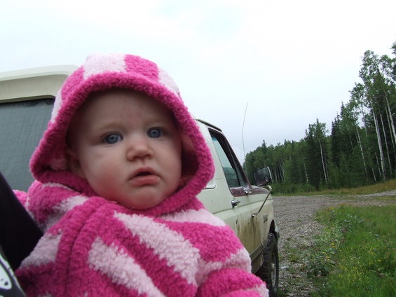 Baby in a pink and white striped hoodie sits in a vehicle, looking out at a wooded area