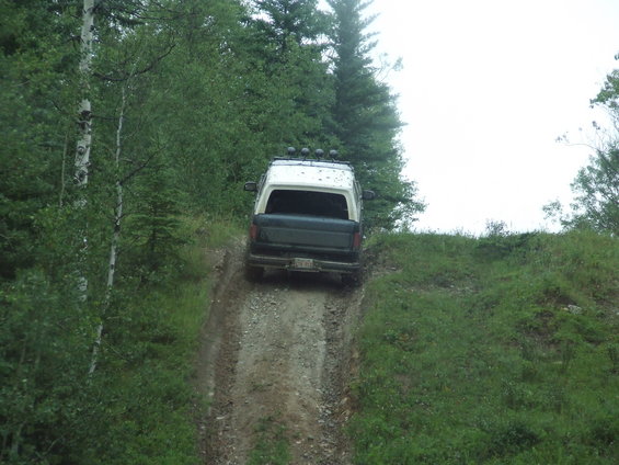 Dark blue and white Ford Bronco driving up a dirt hill, rear view