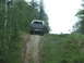 1990 Ford Bronco - A dark blue SUV with a white top navigates a steep dirt incline surrounded by lush green foliage.