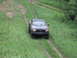1990 Ford Bronco - A dark pickup truck navigates a muddy track through tall grass.