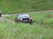 1990 Ford Bronco - A dark gray Ford F-Series truck navigates a grassy, off-road terrain with another vehicle partially visible to the left.